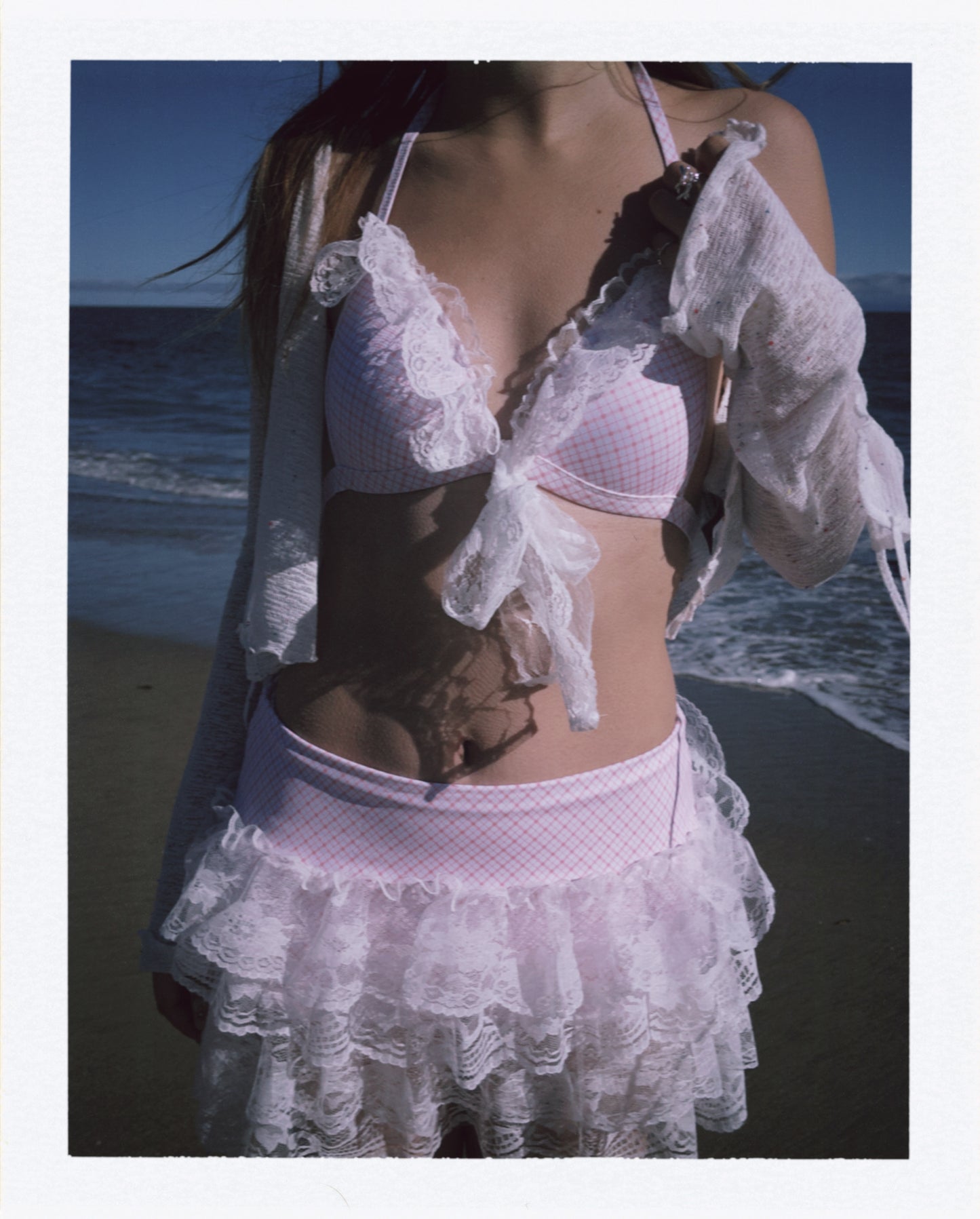 Person wearing a pink bikini with a lace cover-up on a beach.